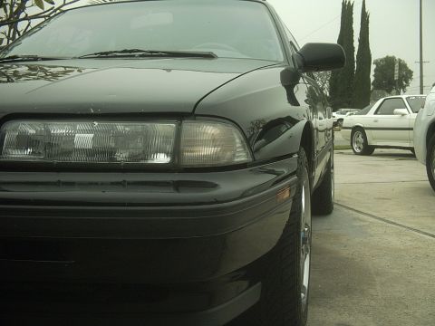 1989 Mazda MX-6 - Front corner view of a black 1989 Mazda MX-6 parked outdoors with another white car visible in the background.