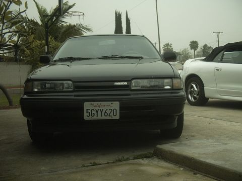 1989 Mazda MX-6 - Front view of a black 1989 Mazda MX-6 parked next to a white convertible.