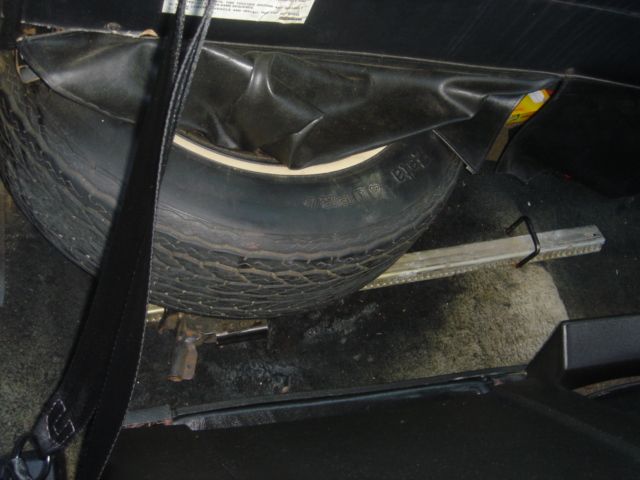 Whitewall spare tire and bumper jack in open trunk spare well with vinyl cover pulled back
