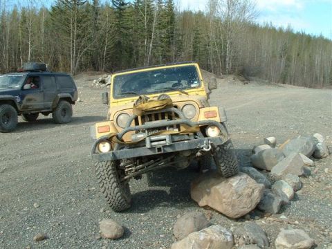 2000 Jeep TJ - A yellow Jeep Wrangler navigates a rocky obstacle course with another SUV in the background.