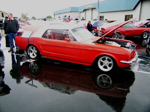 2002 Ford Mustang - A classic red convertible with its hood up is displayed on a wet surface, with other vehicles visible in the background.