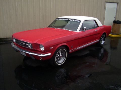 2002 Ford Mustang - A red 1965 Ford Mustang coupe with a white roof is parked on a wet surface outside a building.