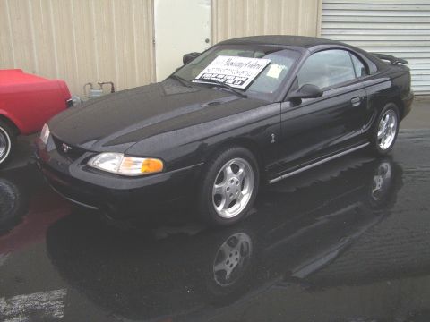 2002 Ford Mustang - A black 2002 Ford Mustang coupe is parked next to a red vehicle, with a sign on the windshield.