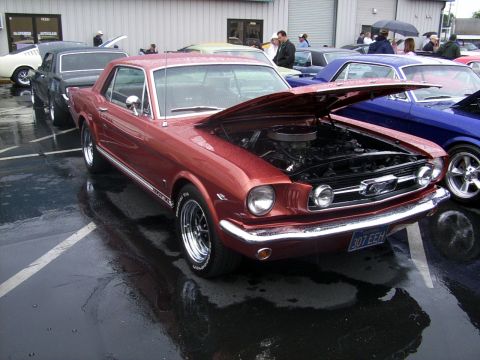2002 Ford Mustang - A red 1965 Ford Mustang coupe is displayed with its hood open, parked in a lot with other vehicles.