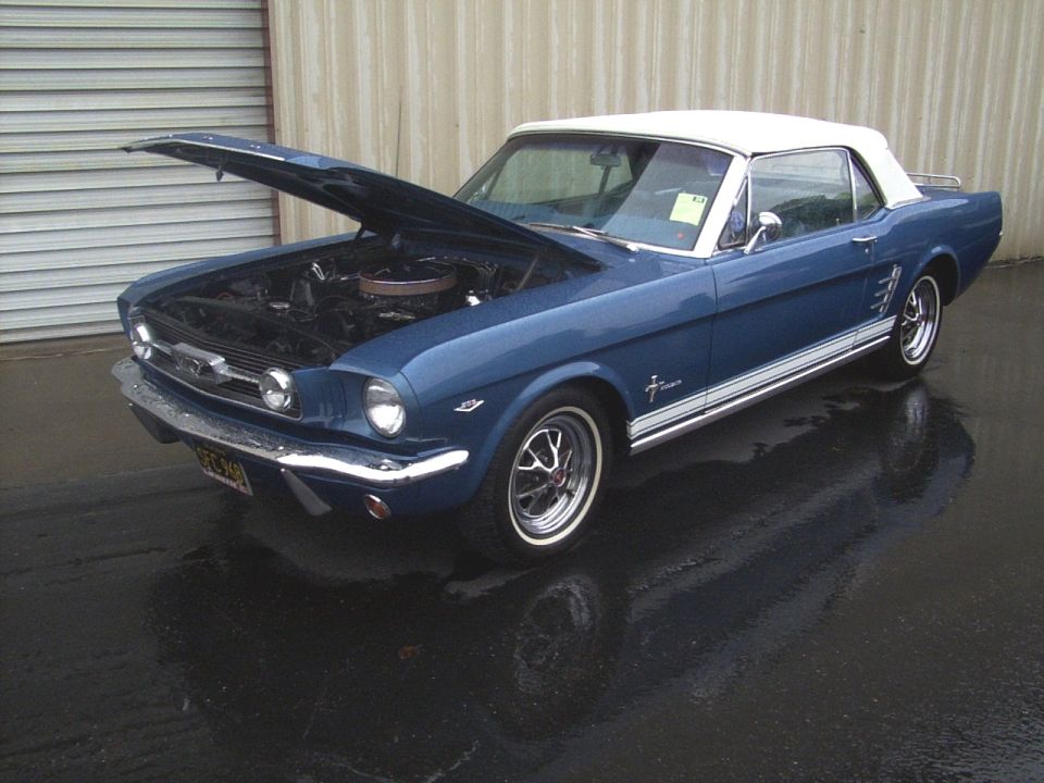 Blue 1965 Mustang convertible with white top, hood open, parked on wet pavement