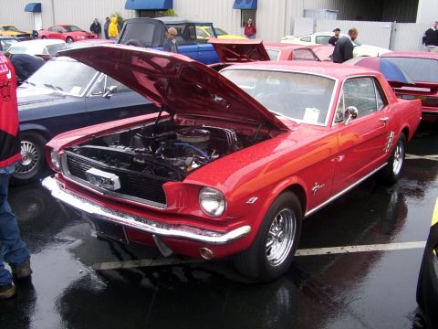 2002 Ford Mustang - A red classic coupe is displayed with its hood open, surrounded by other vehicles and attendees at an outdoor event.