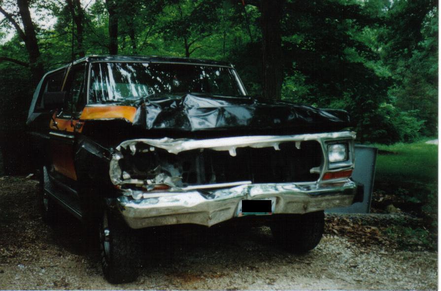 Front view of a heavily damaged black and orange Ford Bronco. Hood is crumpled, grille is missing