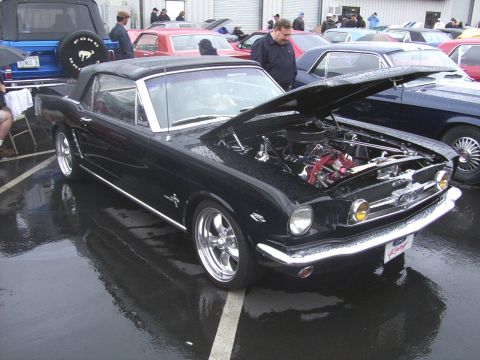 2002 Ford Mustang - A black 1965 Ford Mustang convertible is displayed with its hood open, parked on a wet asphalt lot.