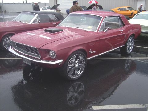 2002 Ford Mustang - This red coupe, identified as a 1967 Mustang, is parked next to another classic car on a wet day.