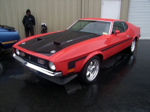 2002 Ford Mustang - A red classic Ford Mustang with a black hood and racing stripes sits on a wet surface outside a building.
