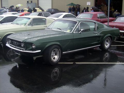 2002 Ford Mustang - A dark green 1967 Ford Mustang fastback is parked outside with other vehicles on a rainy day.