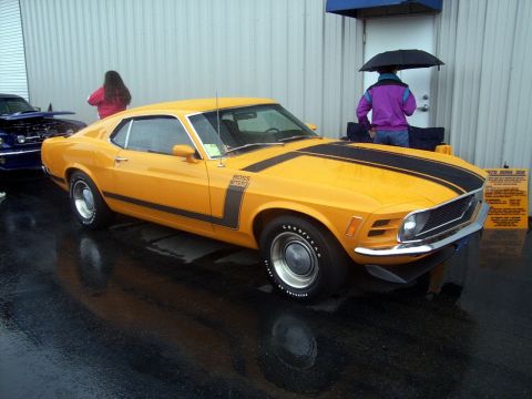2002 Ford Mustang - A yellow 1970 Ford Mustang Boss 302 is displayed outdoors, with another vehicle and onlookers present.