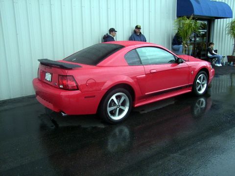 2002 Ford Mustang - A red 2002 Ford Mustang coupe is parked outside a building on a wet day.