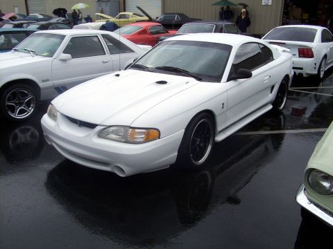 2002 Ford Mustang - White Ford Mustang SN95 generation with hood scoops and black wheels parked outside.