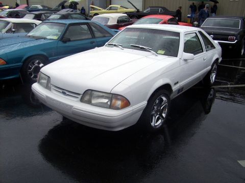 2002 Ford Mustang - A white Ford Mustang hatchback is parked on a wet lot with other vehicles visible.