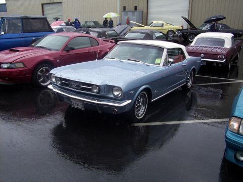 2002 Ford Mustang - A light blue 1965 Ford Mustang convertible is parked on a wet lot, with other vehicles visible in the background.
