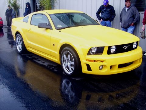 2002 Ford Mustang - A bright yellow Ford Mustang is parked outside on a wet surface, reflecting the car and the surroundings.