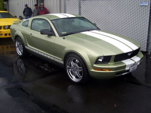2002 Ford Mustang - A green Ford Mustang with white racing stripes is parked next to a yellow car.