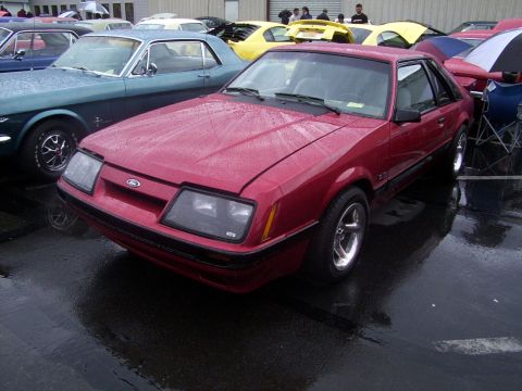 2002 Ford Mustang - Red Ford Mustang from the mid-1980s, parked in a lot with other vehicles.
