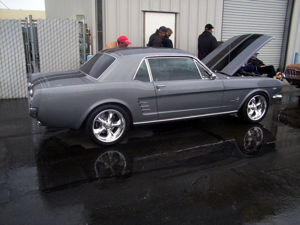 Gray 1965 Ford Mustang coupe with black racing stripes on hood and trunk, chrome wheels, hood open
