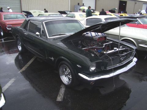 2002 Ford Mustang - A dark green classic Mustang is displayed with its hood open, a prominent supercharger under the engine bay.