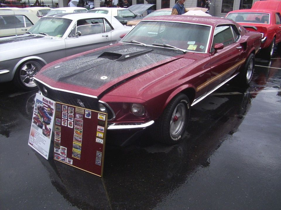 Maroon 1969 Ford Mustang Mach 1 with black hood scoop and stripes, parked next to a white classic car