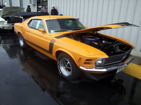 2002 Ford Mustang - A classic orange Mustang Boss 302 is displayed with its hood open, parked on a wet surface next to another vehicle.