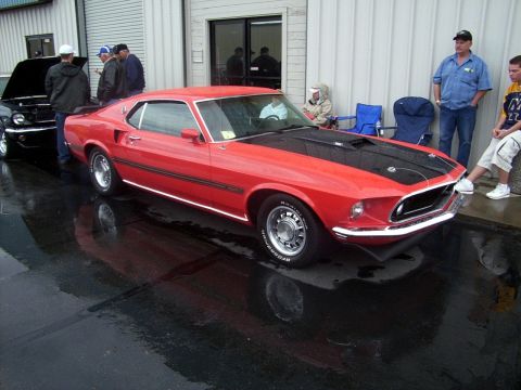 2002 Ford Mustang - A red 1969 Ford Mustang fastback is displayed next to another car, with people standing around.