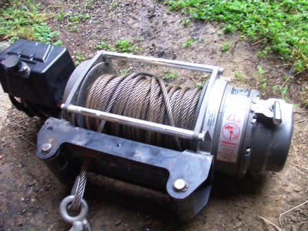 1990 Ford Bronco - A winch with a steel cable and a black control box is shown resting on the ground.