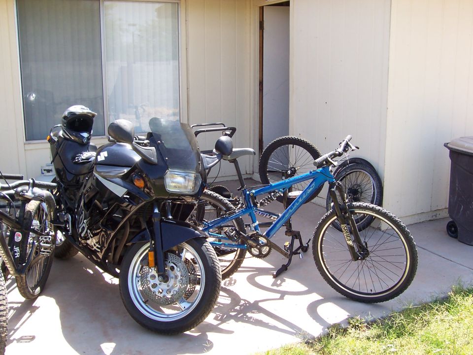 Black Suzuki motorcycle with helmet on tank parked beside a blue mountain bike