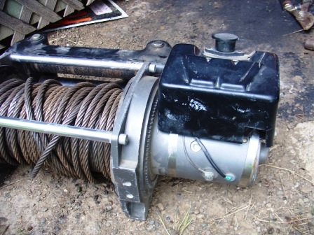 1990 Ford Bronco - A winch with a thick steel cable is shown up close, resting on the dirt.