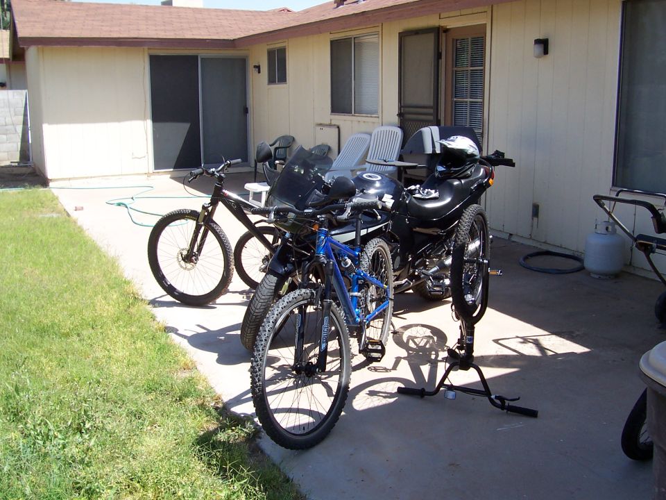 Two bicycles and a motorcycle parked on a concrete patio next to a house
