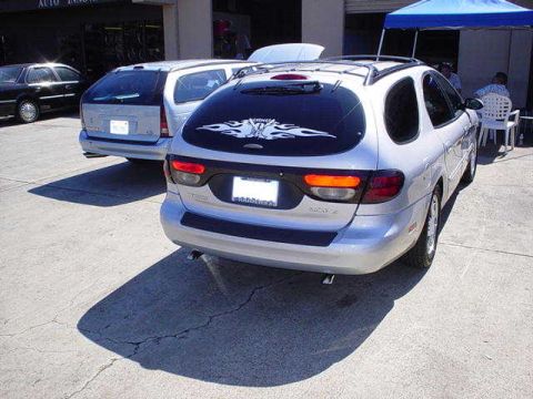 2002 Ford Taurus - A silver 2002 Ford Taurus wagon is seen from the rear, flame decals on its back window and parked next to another wagon.