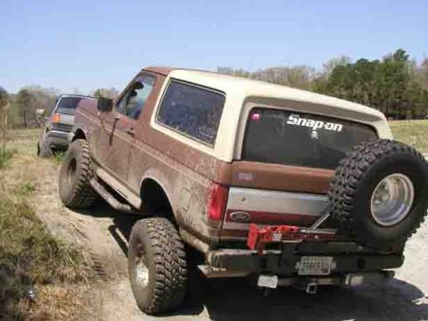 1988 Ford Bronco - A lifted Ford Bronco navigates a muddy trail with another vehicle following close behind.
