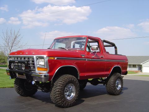 1978 Ford Bronco - A red 1978 Ford Bronco is parked on a paved surface under a blue sky with scattered clouds.