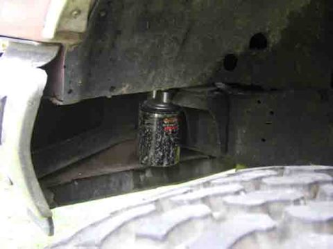 1988 Ford Bronco - A black spin-on oil filter mounted on a remote filter adapter tucked up inside the inner fender well, shot from below past a knobby mud-ter…