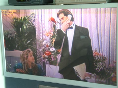 1990 Ford Bronco - A television displays a scene with a man in a tuxedo and a young woman, set against a backdrop of floral arrangements and curtains.