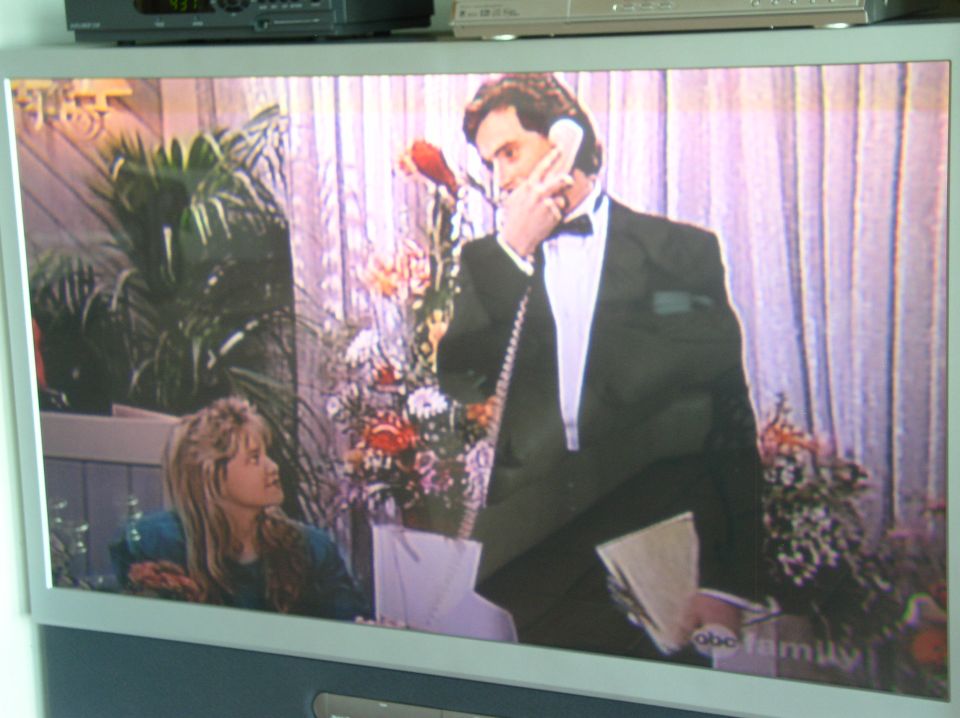 Television screen displaying a scene with a man in a tuxedo on the phone and a young woman looking on