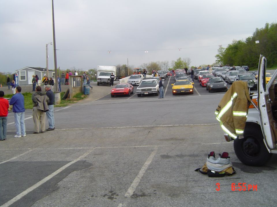 Parking lot scene with many cars and people gathered