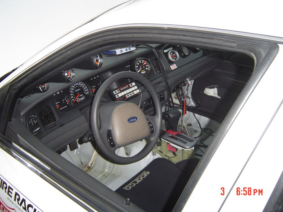 White car interior with racing seat, aftermarket gauges, and a Ford steering wheel