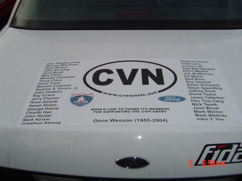 1999 Ford Crown Victoria - The rear of a white car displays a large sticker with 'CVN' and a list of names, along with Ford and Supermotors branding.
