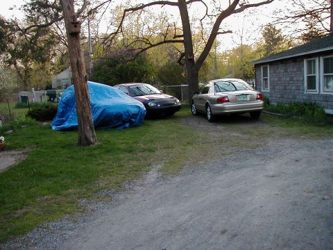 1997 Ford Taurus - A gold sedan is parked in a driveway next to a black car and a vehicle covered by a blue tarp.
