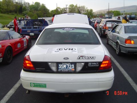 1999 Ford Crown Victoria - A white 1999 Ford Crown Victoria is parked with its hood open, showing other vehicles in the background.