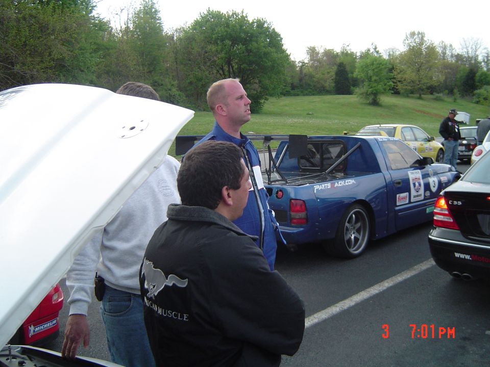 Blue pickup truck with racing modifications and roll cage, parked next to other cars