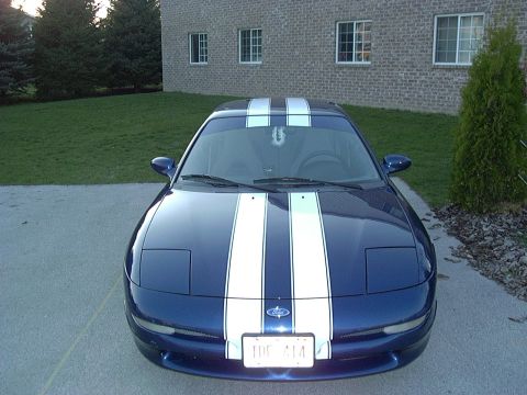 1995 Ford Probe - A blue 1995 Ford Probe with white racing stripes is parked in front of a brick building.