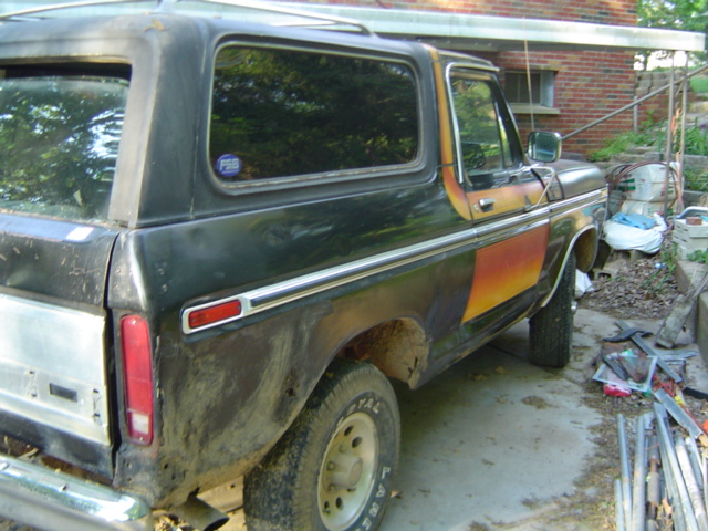 Side view of a dark green Ford Bronco with orange and yellow stripe accents. It's parked outside a brick building