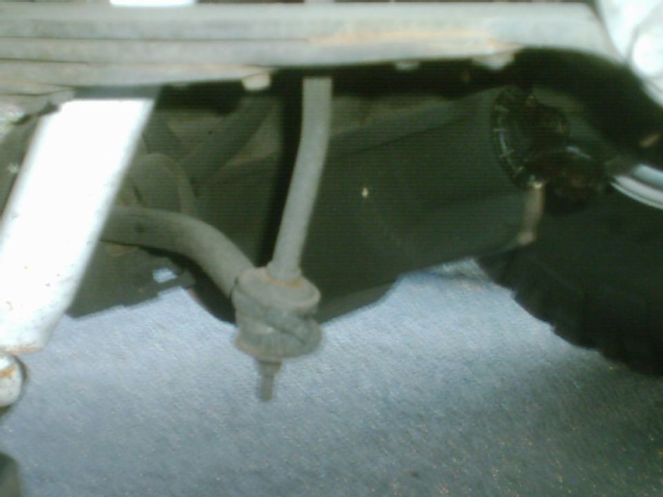 Blurry under-dash view of a rod through a rubber floor boot above gray carpet