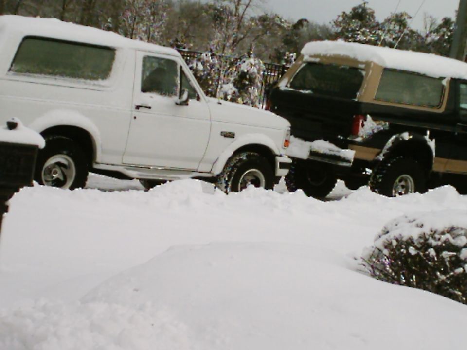 White and two-tone Ford Broncos covered in snow in a driveway