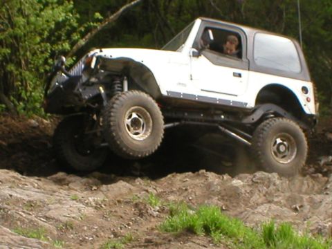 1978 Ford Bronco - A white Jeep Wrangler tackles a challenging off-road course with one wheel in the air.