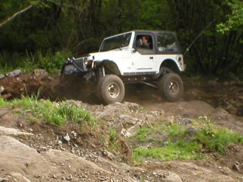 1978 Ford Bronco - A white Jeep Wrangler navigates a rocky, off-road trail, kicking up dirt.